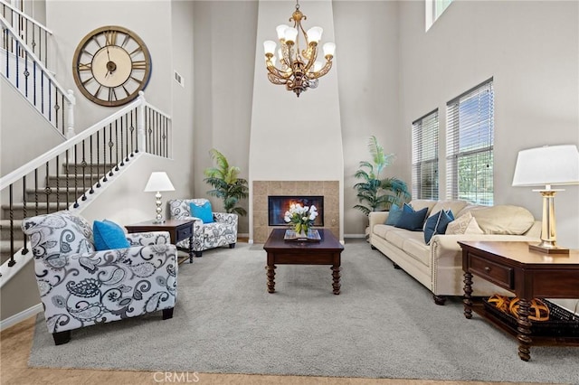 living room featuring an inviting chandelier, a towering ceiling, carpet floors, and a tile fireplace