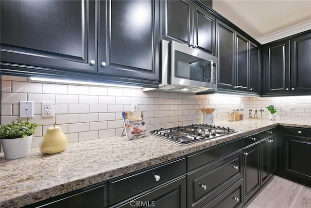 kitchen featuring stainless steel appliances, light stone countertops, light wood-type flooring, and decorative backsplash