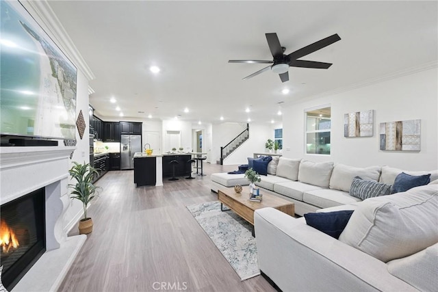 living room with ornamental molding, ceiling fan, and light wood-type flooring