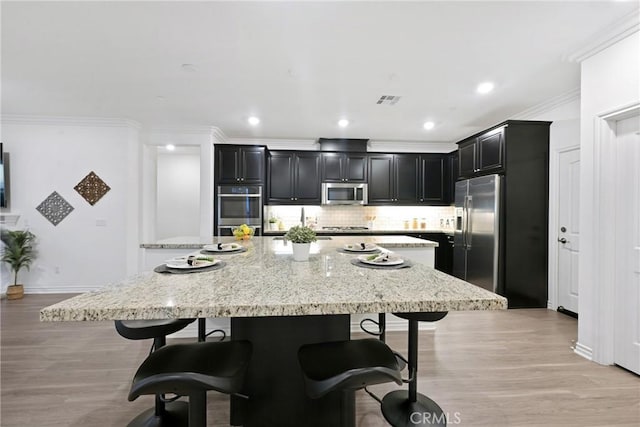 kitchen featuring a breakfast bar area, light stone counters, appliances with stainless steel finishes, a kitchen island, and decorative backsplash