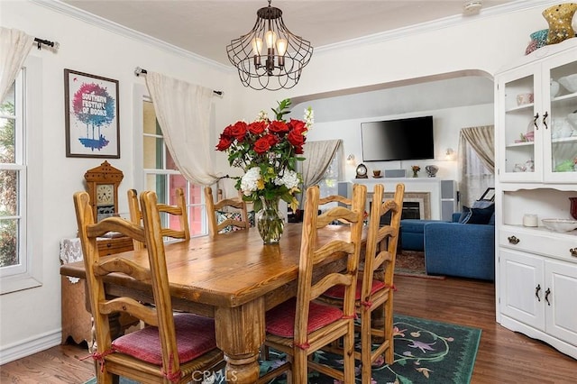 dining area featuring ornamental molding, a chandelier, a fireplace, and dark wood finished floors