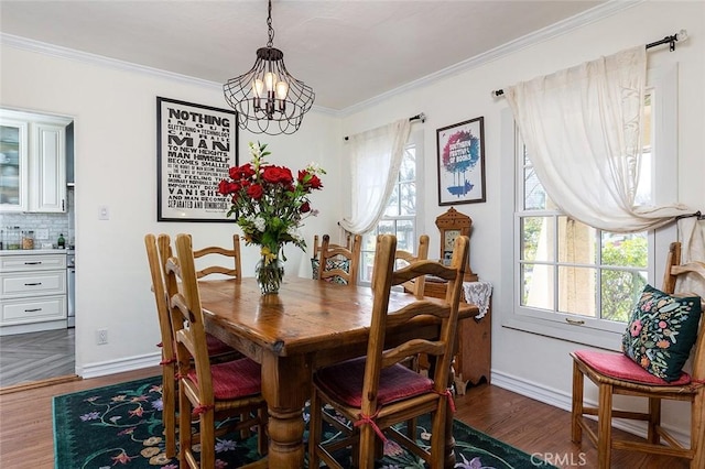 dining space with dark wood-type flooring, crown molding, baseboards, and an inviting chandelier