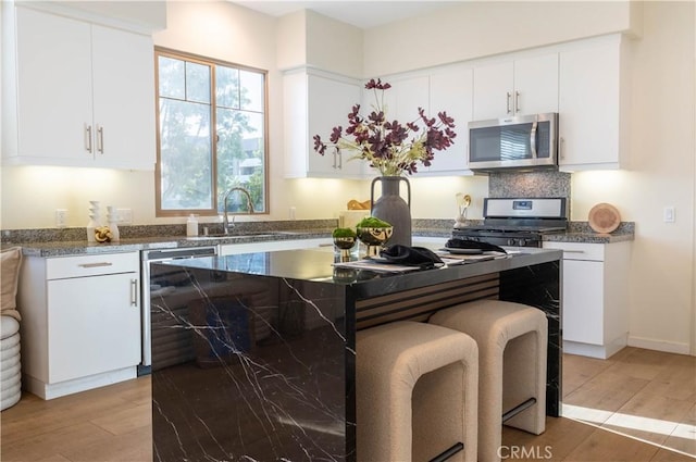 kitchen featuring stainless steel appliances, wood finished floors, a kitchen island, a sink, and white cabinets