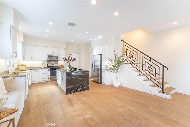 kitchen featuring light wood finished floors, stainless steel appliances, visible vents, white cabinets, and light stone countertops