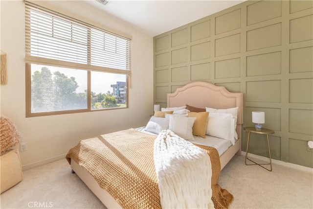 bedroom featuring an accent wall, light carpet, a decorative wall, and baseboards