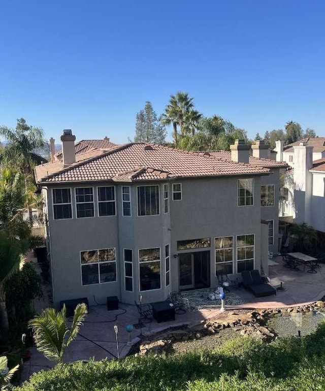 rear view of property with stucco siding, a chimney, and a patio