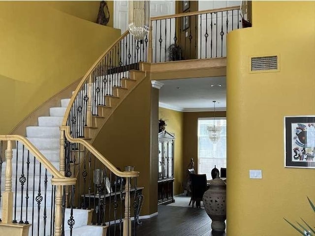 stairs with ornamental molding, visible vents, a towering ceiling, and an inviting chandelier