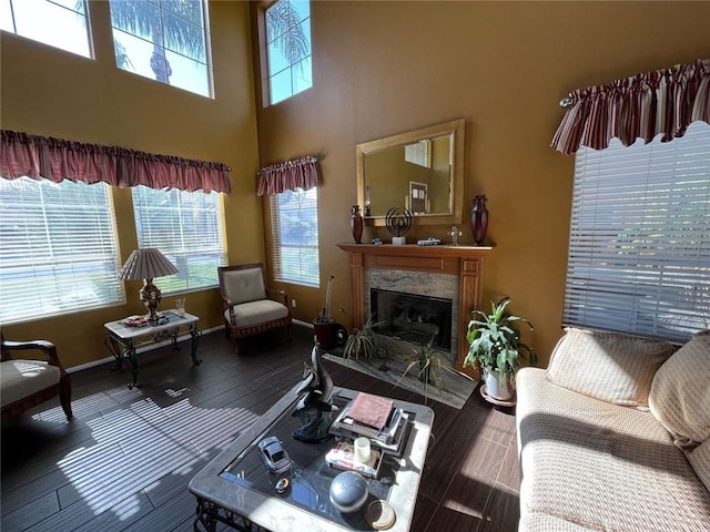 living area featuring a high end fireplace, a towering ceiling, baseboards, and wood finished floors