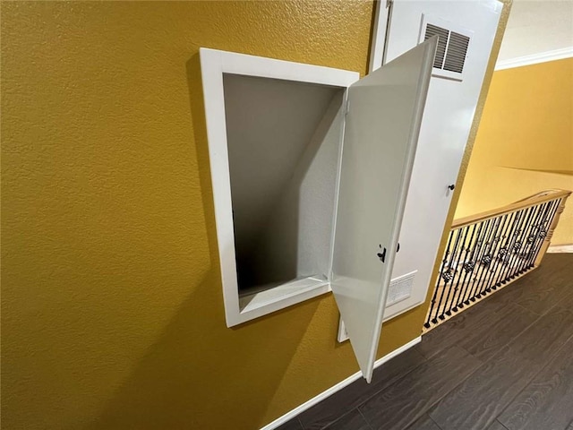 interior space with crown molding, visible vents, a textured wall, wood finished floors, and baseboards