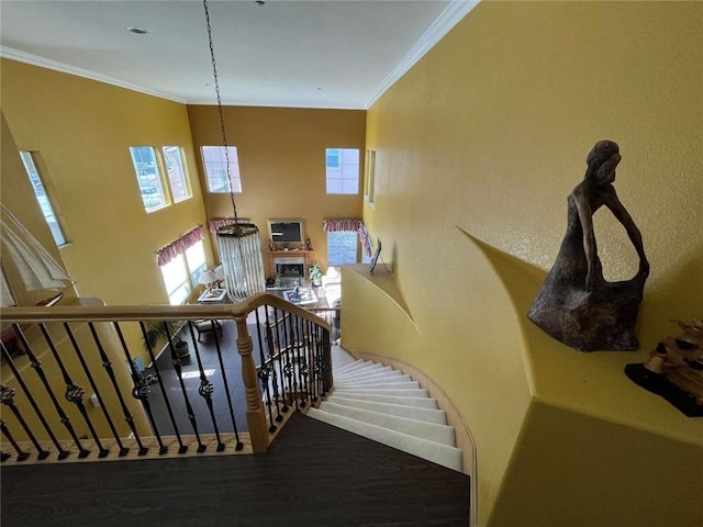 stairway with a fireplace, wood finished floors, and crown molding