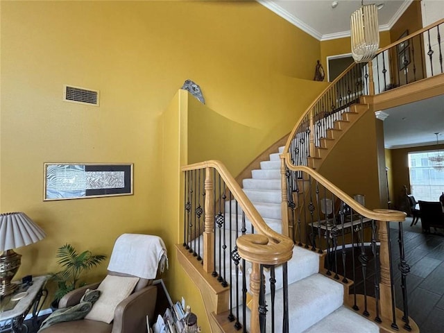 staircase featuring crown molding, a notable chandelier, visible vents, a high ceiling, and wood finished floors