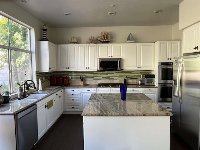 kitchen with light stone counters, stainless steel appliances, a sink, white cabinets, and tasteful backsplash