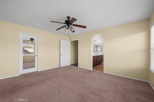 unfurnished bedroom featuring arched walkways, ceiling fan, ensuite bathroom, carpet floors, and baseboards