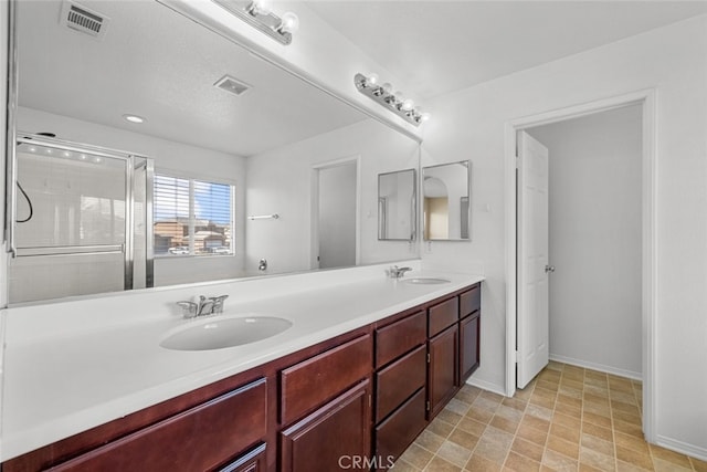 bathroom with double vanity, a shower stall, visible vents, and a sink