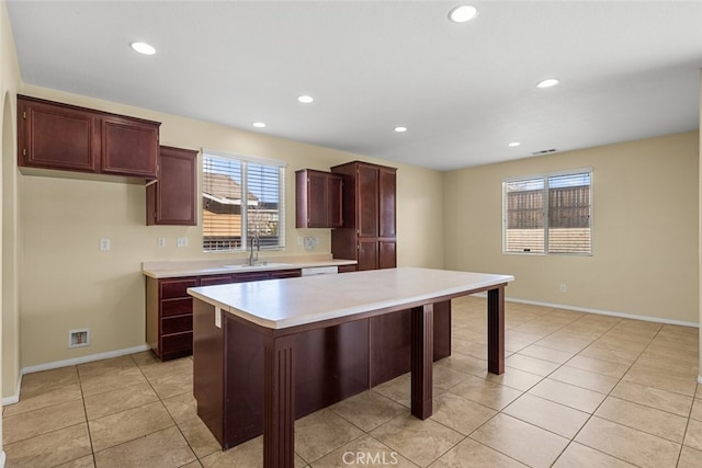 kitchen with light tile patterned floors, a kitchen island, a sink, baseboards, and light countertops