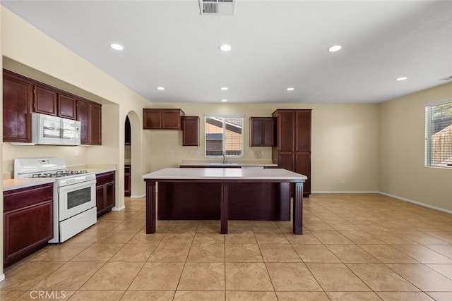 kitchen with white appliances, visible vents, arched walkways, a center island, and light countertops