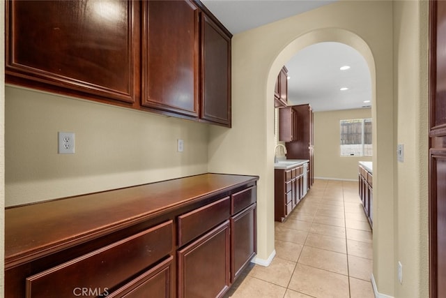 kitchen featuring arched walkways, light tile patterned floors, dark countertops, recessed lighting, and a sink