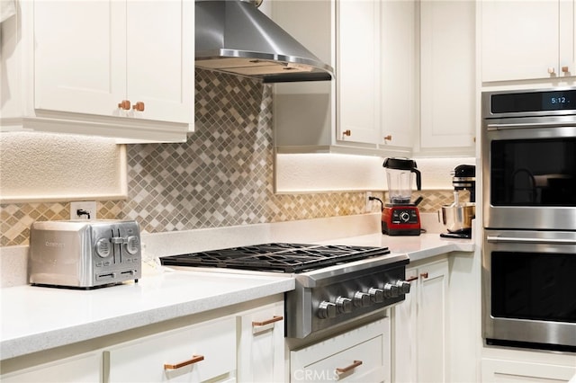 kitchen with appliances with stainless steel finishes, tasteful backsplash, light stone countertops, white cabinets, and range hood