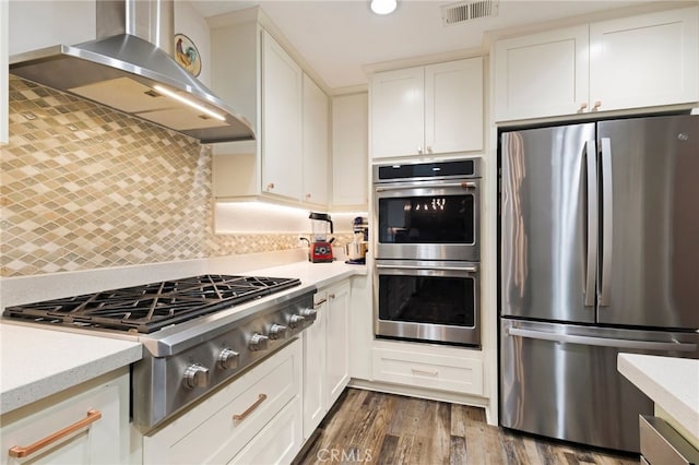 kitchen with tasteful backsplash, wall chimney exhaust hood, stainless steel appliances, dark hardwood / wood-style flooring, and white cabinetry