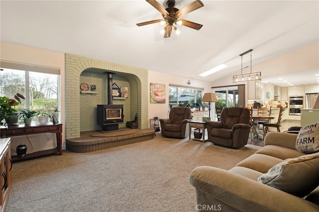 living room with plenty of natural light, vaulted ceiling, a wood stove, and light colored carpet