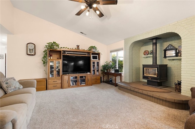 living room with vaulted ceiling, carpet floors, a wood stove, ceiling fan, and brick wall