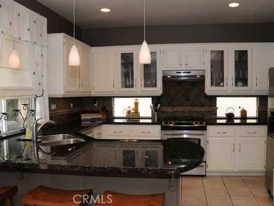 kitchen featuring extractor fan, a breakfast bar, stainless steel stove, dark stone countertops, and white cabinets