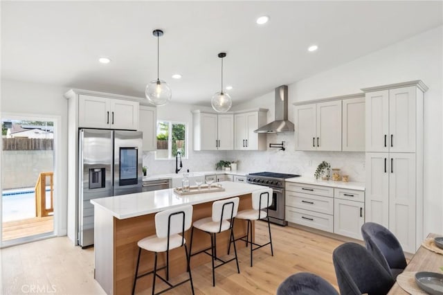 kitchen featuring wall chimney exhaust hood, a center island, a kitchen breakfast bar, pendant lighting, and stainless steel appliances