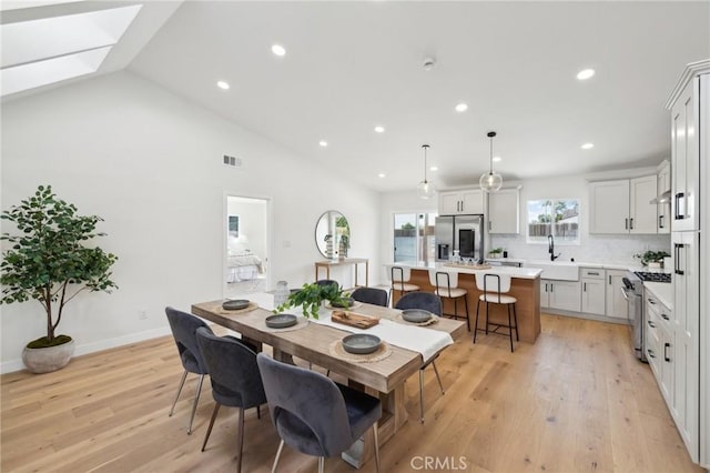 dining space with vaulted ceiling, sink, and light hardwood / wood-style flooring