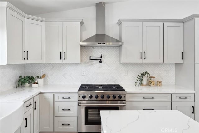 kitchen featuring wall chimney range hood, white cabinetry, light stone counters, tasteful backsplash, and high end stove