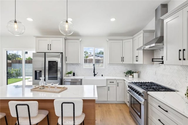 kitchen with appliances with stainless steel finishes, sink, pendant lighting, and wall chimney exhaust hood