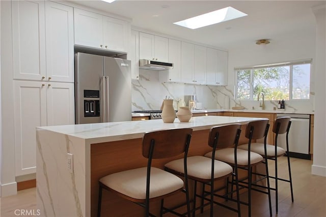 kitchen with appliances with stainless steel finishes, white cabinetry, a kitchen bar, decorative backsplash, and a center island