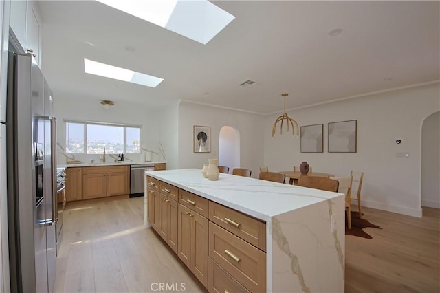 kitchen featuring a skylight, stainless steel appliances, a center island, light stone counters, and light hardwood / wood-style floors