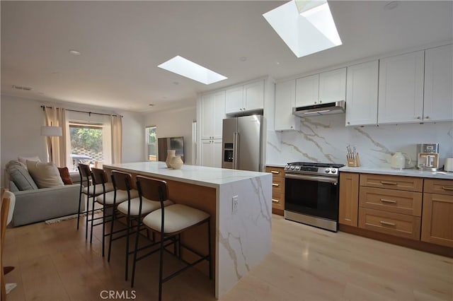 kitchen featuring light stone counters, light wood-type flooring, appliances with stainless steel finishes, a kitchen island, and white cabinets