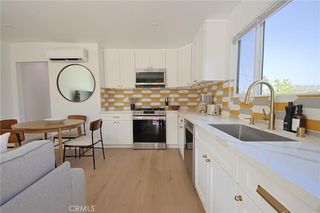 kitchen with sink, appliances with stainless steel finishes, a wall unit AC, light stone countertops, and white cabinets