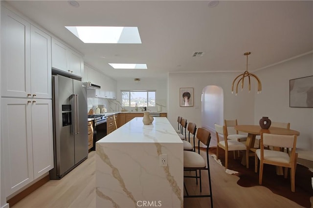 kitchen with decorative light fixtures, white cabinets, a center island, stainless steel appliances, and light stone countertops