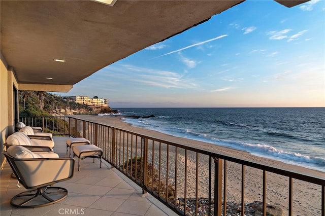 balcony at dusk featuring a water view and a view of the beach