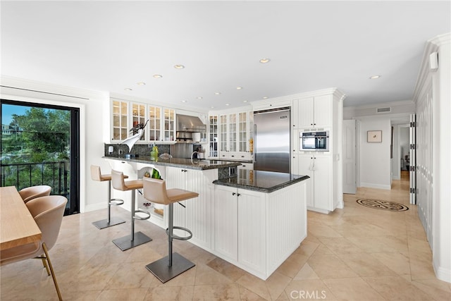 kitchen featuring wall chimney exhaust hood, a breakfast bar area, white cabinetry, crown molding, and built in fridge