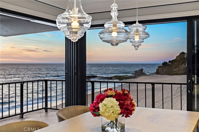 balcony at dusk featuring a water view and a view of the beach