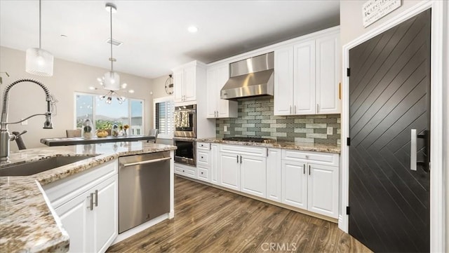 kitchen with dark wood-style floors, stainless steel appliances, white cabinets, a sink, and wall chimney range hood