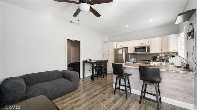 kitchen with stainless steel appliances, decorative backsplash, white cabinets, wood finished floors, and a peninsula