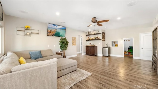 living area with arched walkways, recessed lighting, wood finished floors, baseboards, and a dry bar