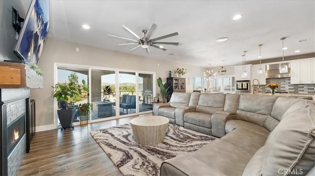 living room featuring ceiling fan with notable chandelier, wood finished floors, plenty of natural light, and a glass covered fireplace