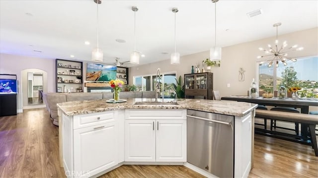 kitchen featuring arched walkways, stainless steel dishwasher, open floor plan, a sink, and light wood-type flooring