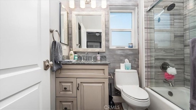 bathroom with shower / bath combination with glass door, vanity, toilet, and tile walls