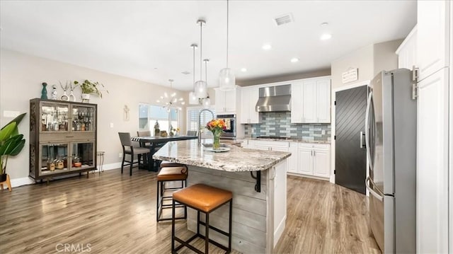 kitchen with light wood finished floors, white cabinets, stainless steel appliances, wall chimney range hood, and backsplash