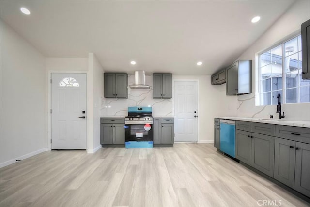 kitchen with gray cabinetry, stainless steel appliances, light hardwood / wood-style floors, and wall chimney exhaust hood