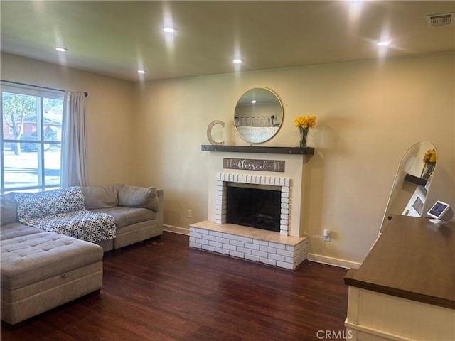 living room with a brick fireplace, baseboards, visible vents, and dark wood finished floors