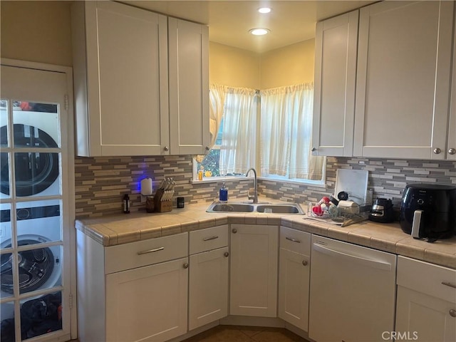 kitchen featuring stacked washer and dryer, white dishwasher, a sink, and white cabinets