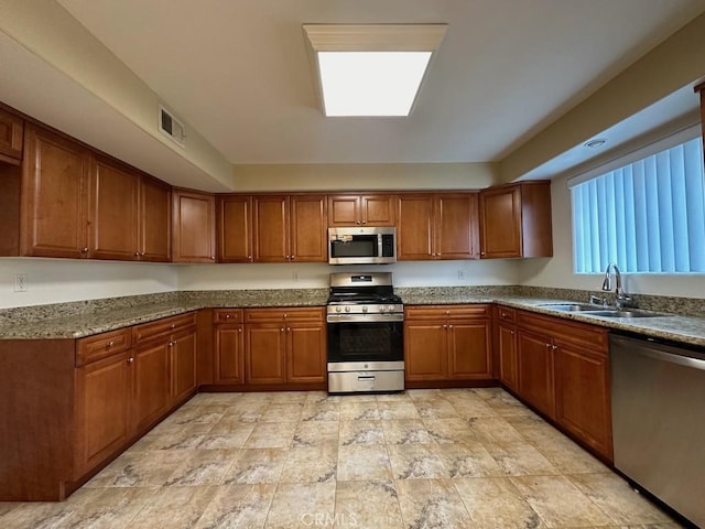 kitchen with appliances with stainless steel finishes, a skylight, sink, and stone counters