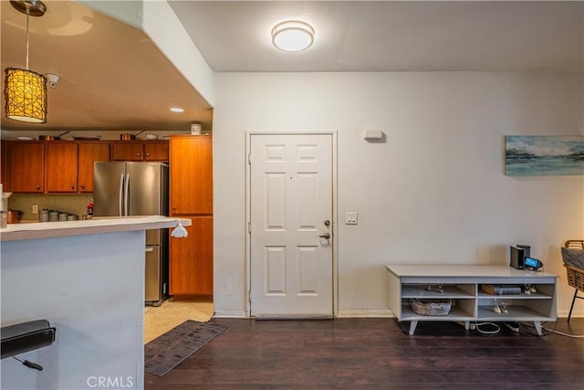 kitchen with brown cabinetry, dark wood-type flooring, freestanding refrigerator, light countertops, and pendant lighting